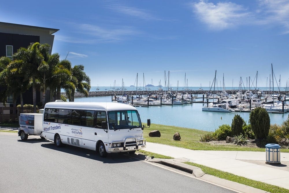 a white bus driving down a street next to a marina.
