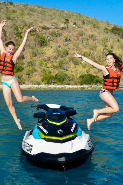 two girls jumping off a jet ski in the water.
